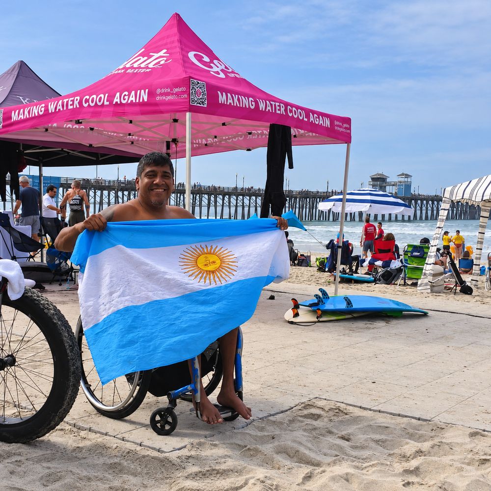 Surfista en silla de ruedas sonriendo con la bandera argentina