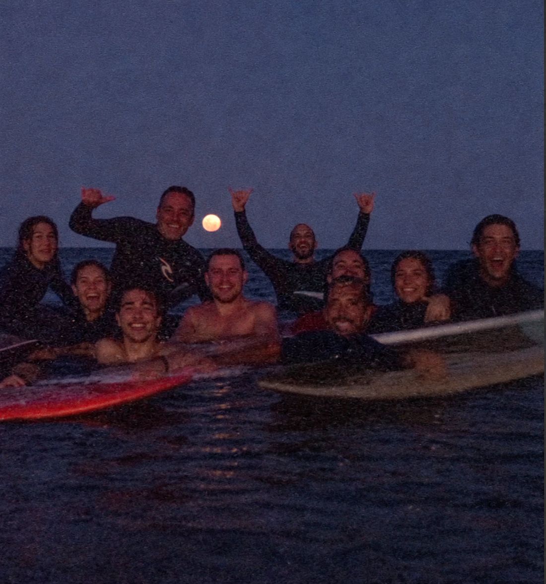 Alumnos e instructores de Buenas Olas en el agua con la luna llena de fondo